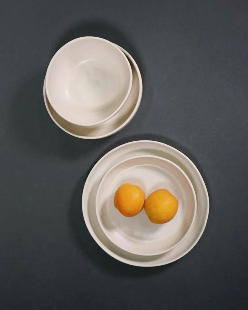 off-white nested dinnerware pieces with two oranges on a dark gray background