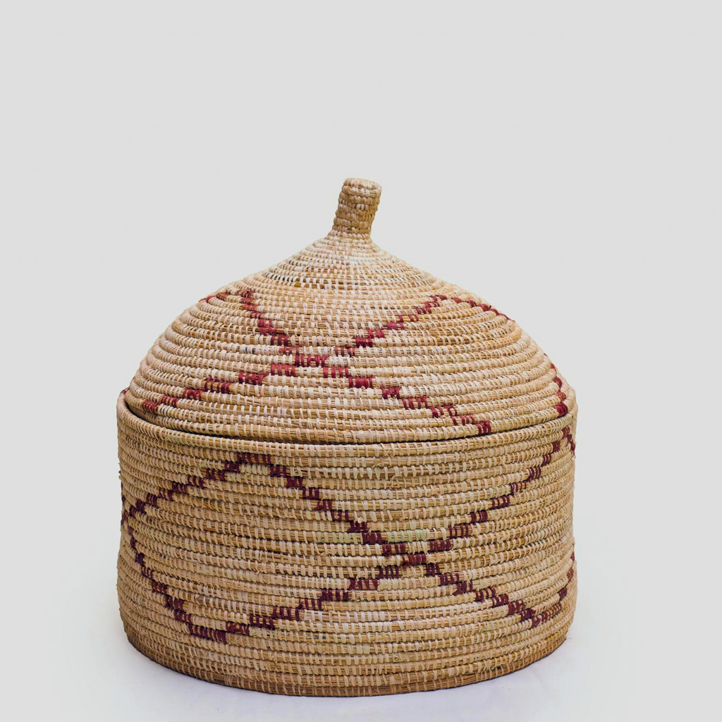 Woven basket with peaked lid in a natural light brown color with minimal red diamond design accent woven on the base and lid.