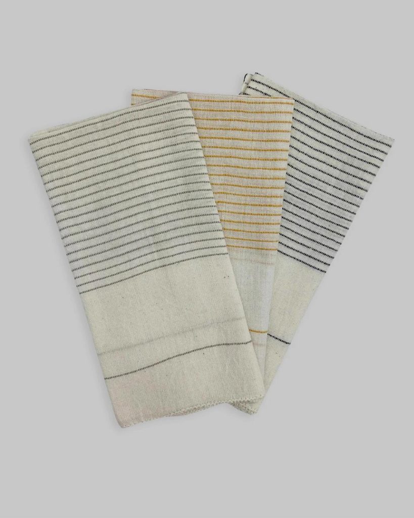 Three folded off-white napkins in fanned out display, one with grey stripes, one with yellow stripes, and one with navy stripes