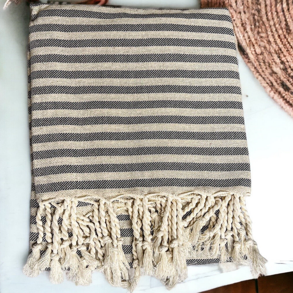 Gray and black striped cotton towel with twisted fringe folded on a white surface